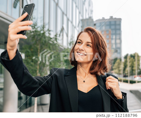 Middle-aged businesswoman with ginger hair taking a selfie while standing outdoors	 112188796