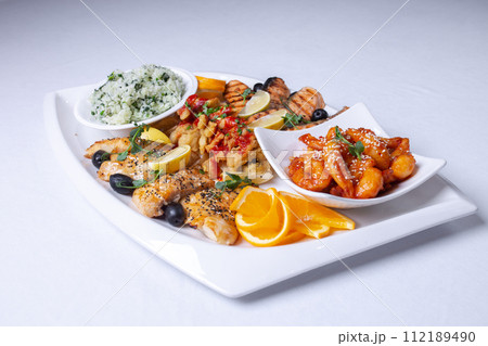 seafood mixture on a white grill. Delicious grilled fish, shrimp in sauce and salmon on the table seafood mixture on a white grill. Delicious grilled fish, shrimp in sauce and salmon on the table 112189490