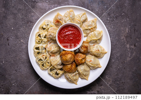 Uzbek samsas and manti with meat, pumpkin and greens on a plate with red sauce 112189497