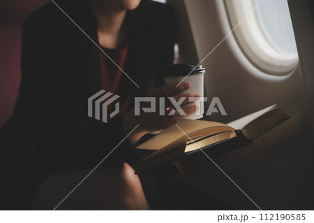 Blonde female tourist checking incoming notification on smartphone sitting on seat of airplane with netbook.Young businesswoman share media from telephone on laptop computer during plane flight 112190585
