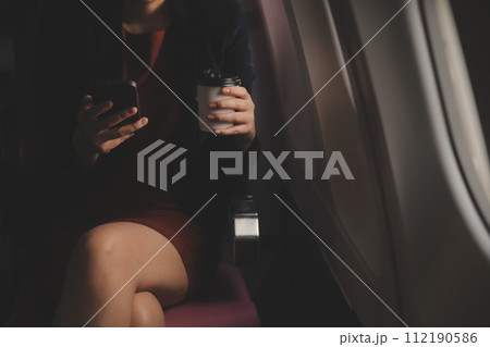 Blonde female tourist checking incoming notification on smartphone sitting on seat of airplane with netbook.Young businesswoman share media from telephone on laptop computer during plane flight Blonde female tourist checking incoming notification on smartphone sitting on seat of airplane with netbook.Young businesswoman share media from telephone on laptop computer during plane flight 112190586