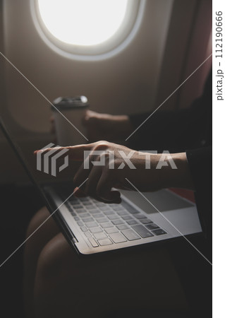 Blonde female tourist checking incoming notification on smartphone sitting on seat of airplane with netbook.Young businesswoman share media from telephone on laptop computer during plane flight 112190666