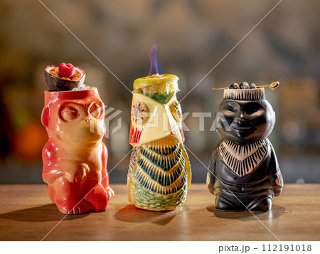 Tiki Drink Cocktails Collection. Set of three tropical tiki cocktails on bar counter. Beautiful tiki cocktails, different decorated with fire flame on bar in night club 112191018