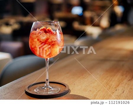 Transparent pink alcohol cocktail in wine glass with ice, aperol and gin on bar counter in restaurant interior. Alcohol drink Aperol Spritz aperitif cocktail. Cold alcoholic cocktail in bar or 112191026