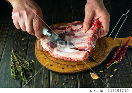 The chef uses a knife to cut the meat from the bone on a kitchen board before preparing the dish. The process of cooking meat on the kitchen table by the hands of a butcher 112191210