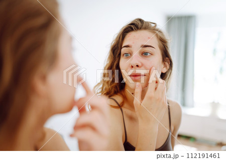 Close-up of a young woman looking at pimples in the mirror. Red spots, rash, acne. Skin treatment. Close-up of a young woman looking at pimples in the mirror. Red spots, rash, acne. Skin treatment. 112191461