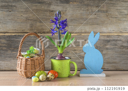 Happy Easter holidays concept; Blue hyacinth in green mug, wicker basket with easter eggs and blue rabbit on a old wooden background Happy Easter holidays concept; Blue hyacinth in green mug, wicker basket with easter eggs and blue rabbit on a old wooden background 112191919