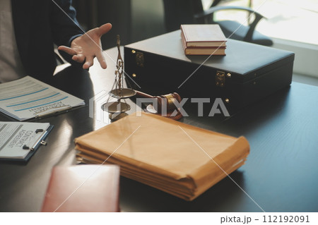 Justice and Law concept. Legal counsel presents to the client a signed contract with gavel and legal law or legal having team meeting at law firm in background 112192091
