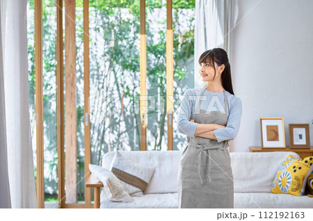 リビングで腕組みするエプロン姿の若い女性 リビングで腕組みするエプロン姿の若い女性 112192163
