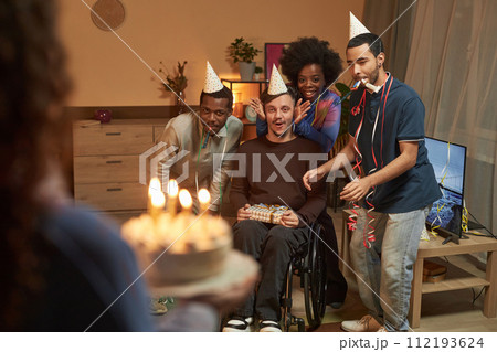 Full length portrait of Birthday surprise for young man with disability friend bringing Birthday cake with candles Full length portrait of Birthday surprise for young man with disability friend bringing Birthday cake with candles 112193624