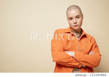 Waist up portrait of bald young woman posing with arms crossed in studio wearing bright orange jacket, copy space Waist up portrait of bald young woman posing with arms crossed in studio wearing bright orange jacket, copy space 112193868