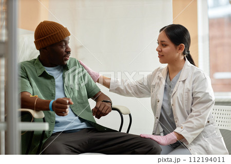 Side view portrait of smiling female doctor comforting patient receiving IV treatment in clinic 112194011