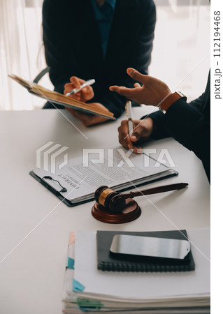 Justice and Law concept. Legal counsel presents to the client a signed contract with gavel and legal law or legal having team meeting at law firm in background 112194468