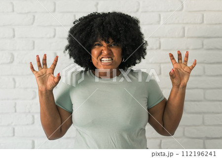 Angry african american woman screaming on brick background. Bad aggressive emotions and premenstrual syndrome or pms concept Angry african american woman screaming on brick background. Bad aggressive emotions and premenstrual syndrome or pms concept 112196241