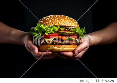 Two hands holding a juicy burger with lettuce, cheese, and tomatoes. Two hands holding a juicy burger with lettuce, cheese, and tomatoes. 112196329