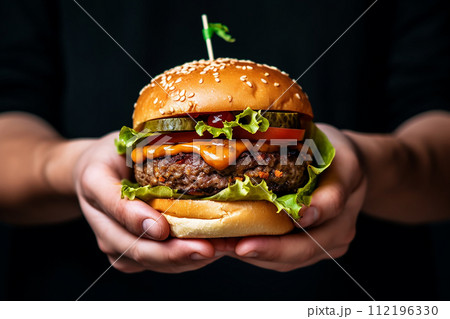 Two hands holding a juicy burger with lettuce, cheese, and tomatoes. 112196330