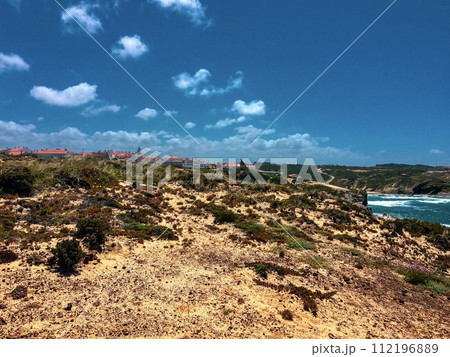 Houses with orange roofs line the top of a rugged cliff under a sky with few clouds. Houses with orange roofs line the top of a rugged cliff under a sky with few clouds. 112196889