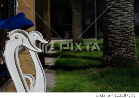 A bench with two white swans on it is in a park A bench with two white swans on it is in a park 112197573