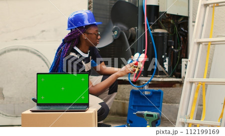 Capable specialist contracted by home owner to detect HVAC system problems, checking real-time superheat and subcooling values measured by manifold gauges displayed on green screen laptop 112199169