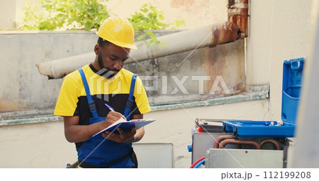 Knowleadgeable engineer doing leak checks and other necessary fixes to prevent major HVAC system failures. Efficient technician verifying air conditioner, writing findings on clipboard Knowleadgeable engineer doing leak checks and other necessary fixes to prevent major HVAC system failures. Efficient technician verifying air conditioner, writing findings on clipboard 112199208