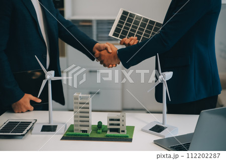 Two Young Engineers Expertise in Solar Cell Installation Meetings and Discussion in The Job. Planning to Install Solar Photovoltaic Panels on Roof Top in The Office Room with Factory Building Plan. 112202287