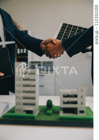 Two Young Engineers Expertise in Solar Cell Installation Meetings and Discussion in The Job. Planning to Install Solar Photovoltaic Panels on Roof Top in The Office Room with Factory Building Plan. 112202288