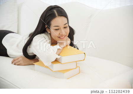 Young asian woman reading book on cozy couch sofa at warm hom. Relax woman holding book read on sofa near window happiness.woman reading open book leisure mind. Happiness woman lifestyle at home 112202439