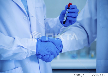 Two asian scientist men team partner shake hands together. Men researcher holding chemistry science tube experiment biotech antibody sample in laboratory. Close up hand corporate coworker partnership 112202449