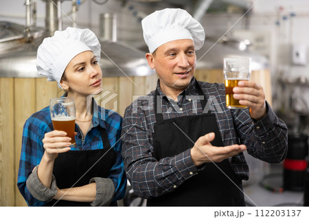 Interested male and female brewers examining quality of beer in brewery 112203137