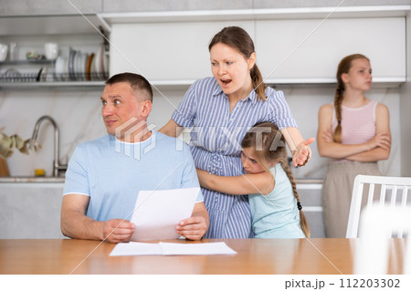 Angry woman chiding upset man sitting with papers in home kitchen 112203302