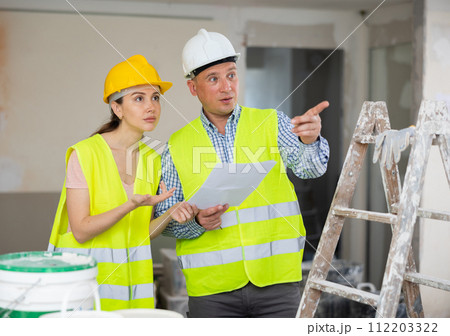 Man and woman builders discussing project documentation Man and woman builders discussing project documentation 112203322
