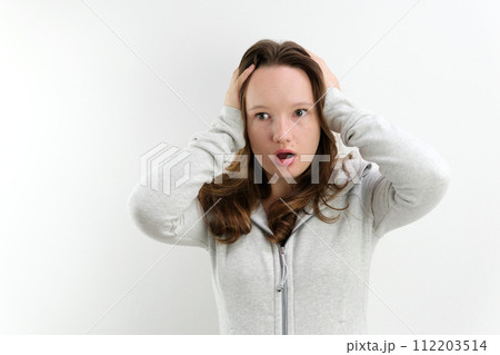 Screaming angry young woman holding her head between hands. horror open your mouth in surprise open your eyes wide hold your head with your hands on a white background teenager great surprise Screaming angry young woman holding her head between hands. horror open your mouth in surprise open your eyes wide hold your head with your hands on a white background teenager great surprise 112203514