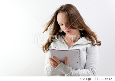 a young teenage girl writes in a large white notebook, she thinks about an essay, comes up with story, young author, adolescence, bites her pen and looks to side, dreams, thinks, plans, writes plans a young teenage girl writes in a large white notebook, she thinks about an essay, comes up with story, young author, adolescence, bites her pen and looks to side, dreams, thinks, plans, writes plans 112203632