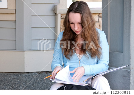 young girl teenager sits on porch in hands with a folder, a magazine and pencil, do homework, solve problems, wait at the door, a beautiful woman, young white jeans, a briefcase, think, work, study 112203911