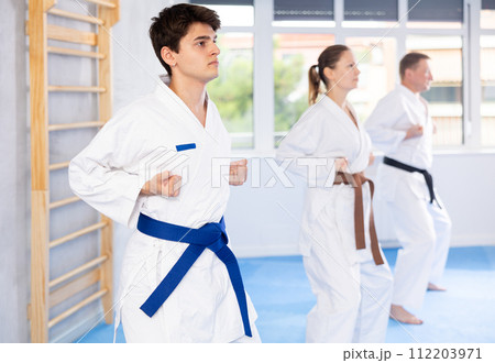 Woman and man in kimono standing in fight stance during group karate training in gym 112203971