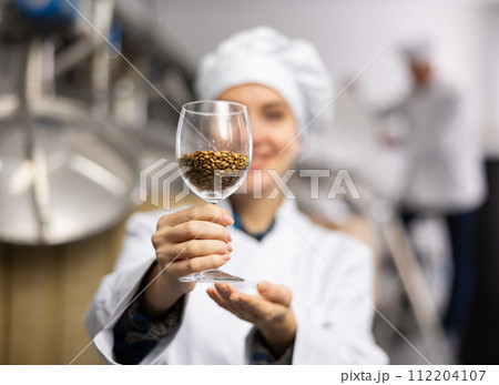 Glass with malted barley grain in hands of female brewmaster 112204107