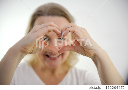 a woman shows her heart with her hands a cheerful look through her hands at the camera white background interest fun joy pleasant emotions happiness 112204472