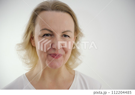 Studio shot of beautiful young woman with blonde hair and naked shoulders. Girl squeeze or blow lips on gray background with copy space for your text or advertising content 112204485