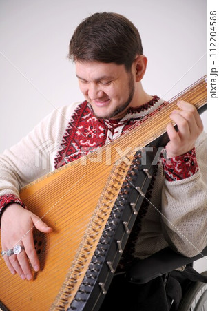 young handsome male Cossack of Ukraine plays the harp and smiles the musician holds the kobza and looks at 30 years old white and red embroidered shirt made of natural fabric Ukrainian symbol young handsome male Cossack of Ukraine plays the harp and smiles the musician holds the kobza and looks at 30 years old white and red embroidered shirt made of natural fabric Ukrainian symbol 112204588