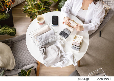 Unrecognizable woman sorting neatly folded linen cotton textile at container and basket on table 112204991