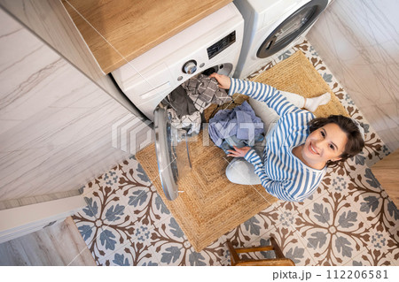 Housewife female taking clean wet clothes fabric from washing machine minimalist bathroom top view Housewife female taking clean wet clothes fabric from washing machine minimalist bathroom top view 112206581