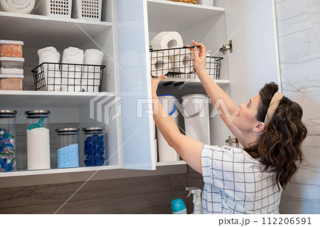 Woman organizing white bathroom laundry comfortable storage on cupboard shelves Woman organizing white bathroom laundry comfortable storage on cupboard shelves 112206591