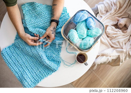 Male hands crochet handmade artwork use wool yarn and hook over table with coffee 112208960
