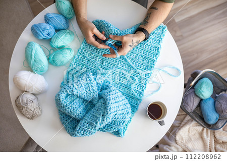Male hands crochet handmade artwork use wool yarn and hook over table with coffee top view 112208962