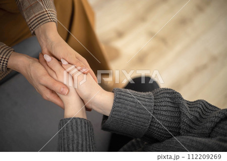 Two woman holding hands to each other concept of support care trust help sisterhood top view closeup 112209269