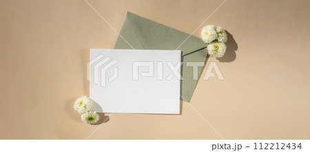 Beautiful little white flowers on postal green envelope on beige background, empty paper note copy space for text, spring time, greeting card for holiday. Flower delivery Beautiful little white flowers on postal green envelope on beige background, empty paper note copy space for text, spring time, greeting card for holiday. Flower delivery 112212434