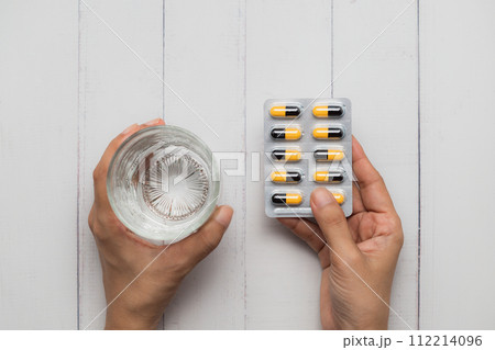 Healthcare Concept with Hand Holding Water and Pills on White Wooden Table 112214096