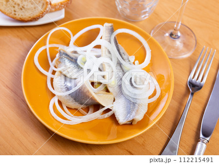 Herring slices served with onions on platter 112215491