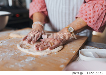 Close up of hands of senior woman preparing traditional easter meals for family, kneading dough for easter cross buns. Recreating family recipes, custom. Close up of hands of senior woman preparing traditional easter meals for family, kneading dough for easter cross buns. Recreating family recipes, custom. 112215545