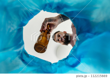 Man throwing glass bottle into recycling bin. Empty alcohol bottle, throwing, New Year's resolutions, drink less alcohol healthy lifestyle without alcoholic drinks. 112215669